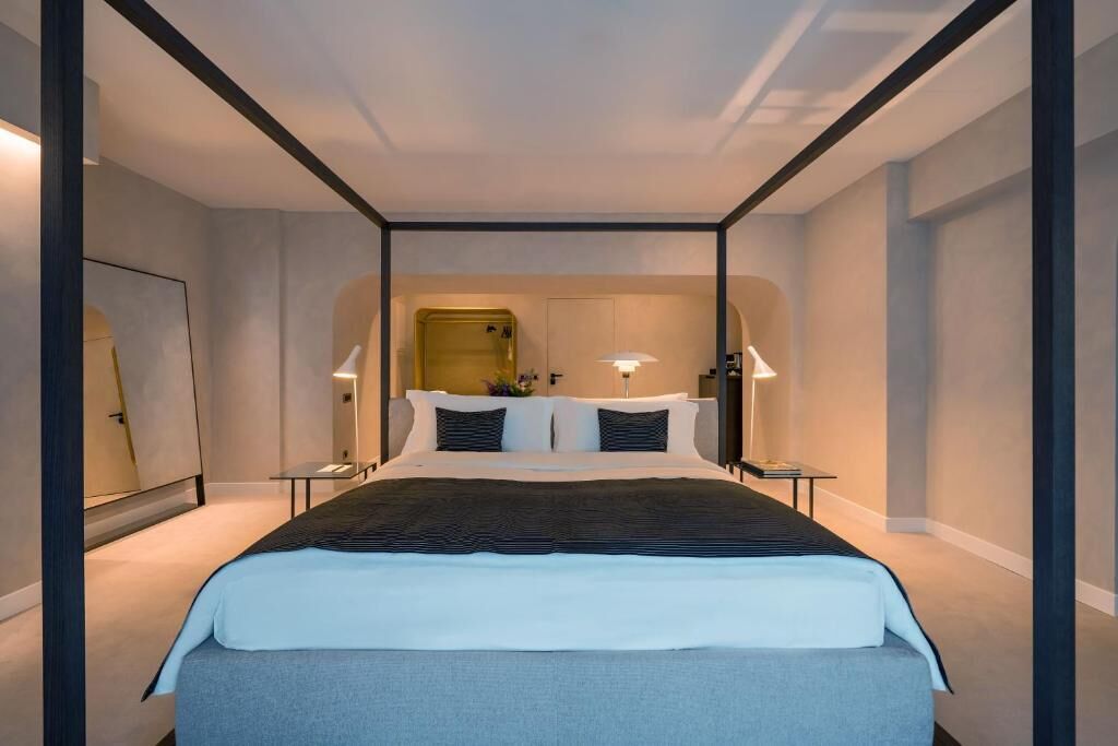 A modern hotel room with a large bed, bedside tables, and a mirror.