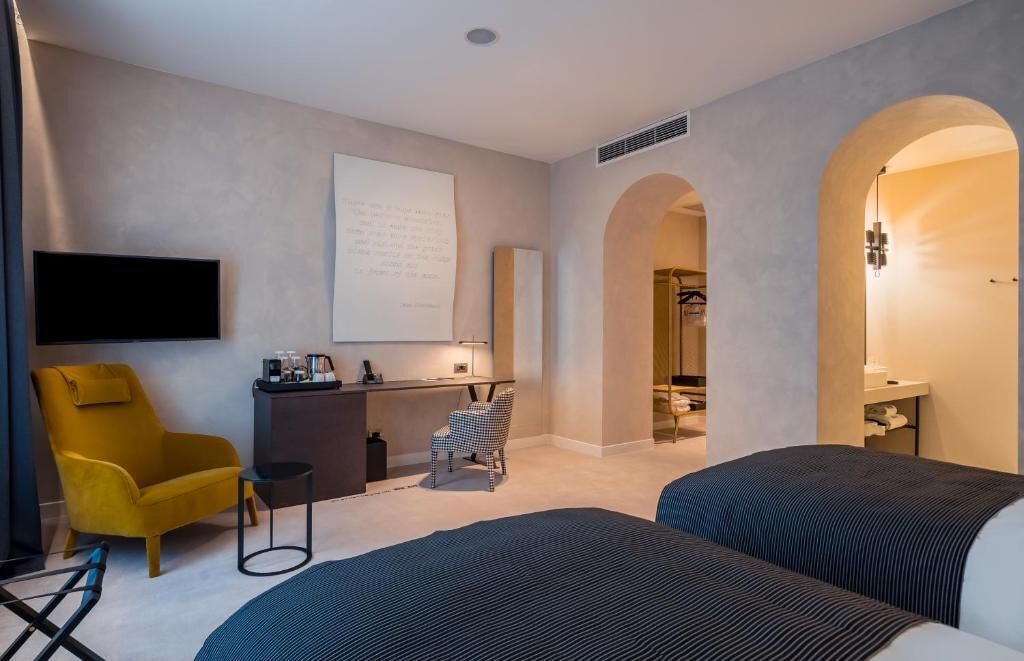 Quarto de hotel moderno com cama, escrivaninha, cadeira e televisão.