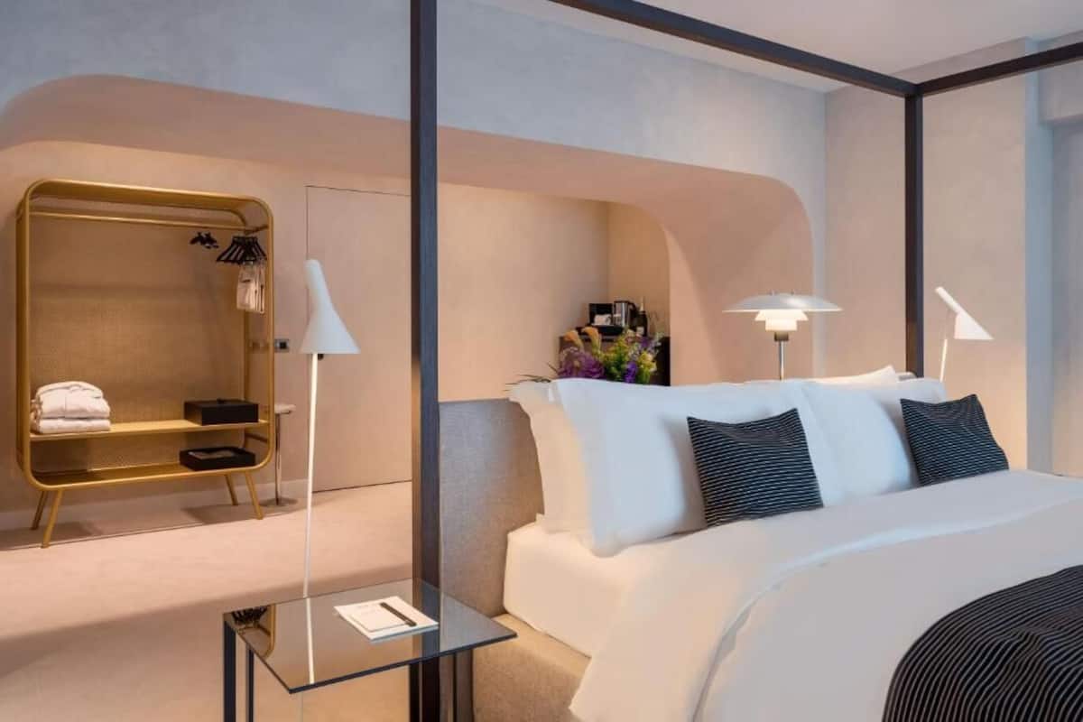 Ett modernt hotellrum med en stor säng, ett soffbord i glas, en sittgrupp med guldfärgad ram och två sänglampor.
