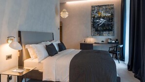 A modern hotel room with a large bed, bedside table, desk, chair, and a painting on the wall. - Monograph Freedom Square (Tbilisi)