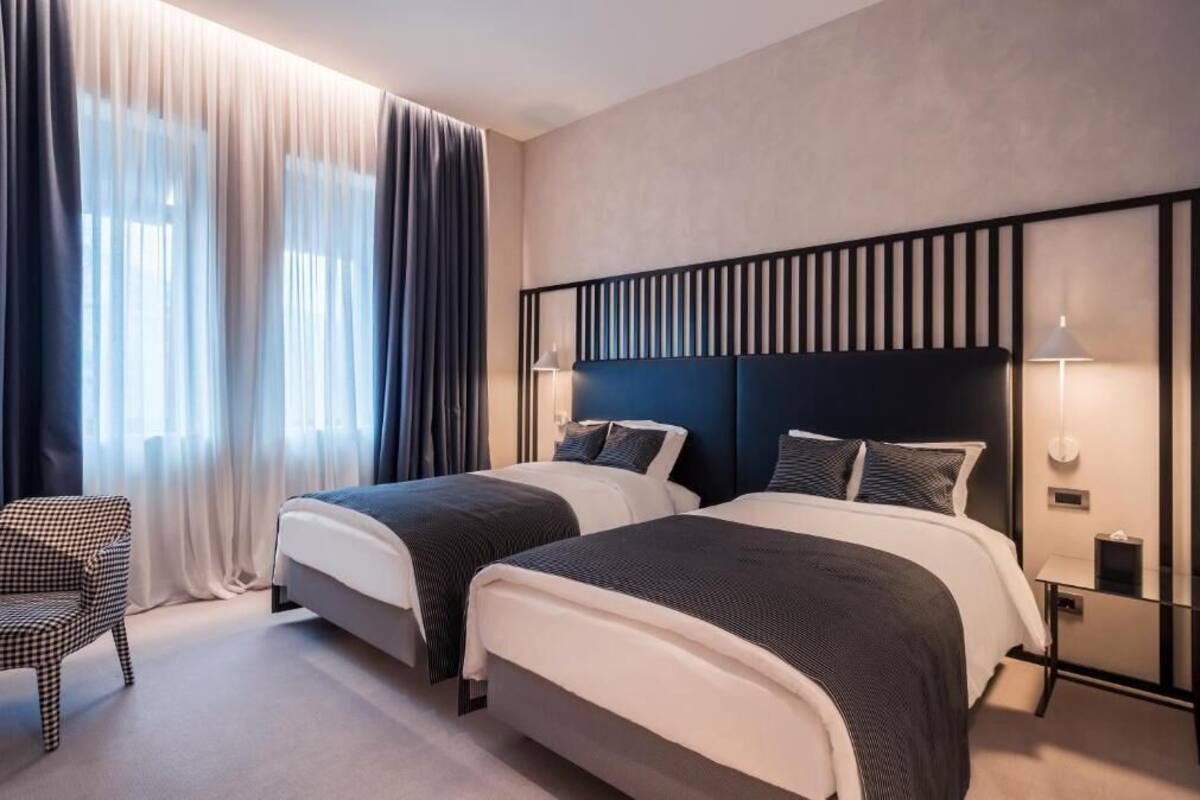 Ett hotellrum med två sängar, en rutig fåtölj, ett sängbord och en lampa.