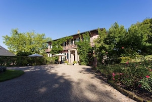 A building with a gravel driveway, a covered outdoor seating area, and lush greenery.