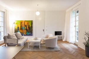 A modern living room with a sofa, armchair, coffee table, and a painting on the wall.