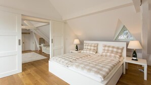 Ein Schlafzimmer mit einem großen Bett, zwei Nachttischen, einem Fenster und einer Treppe, die in einen anderen Raum führt.