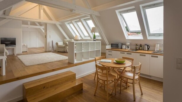 Eine Loftwohnung mit Küche, Essbereich und Wohnraum, der durch hohe Decken und Dachfenster gekennzeichnet ist.