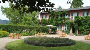Ein rosafarbenes Gebäude mit Garten, Außenbestuhlung und einem runden Rasenkunstwerk.