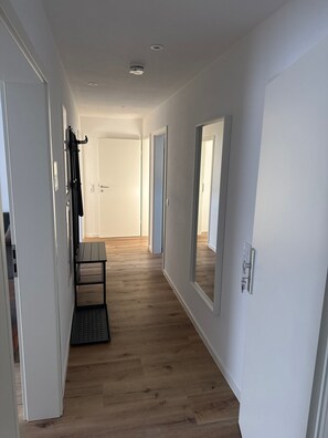 A hallway with wooden flooring, white walls, and doors leading to other rooms.