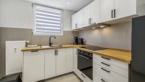 A modern kitchen with white cabinets, a wooden countertop, a stainless steel sink, and a built-in oven. - Apartment 2 (Right) (Mössingen)