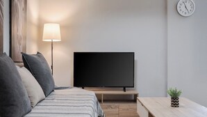 Ein modernes Schlafzimmer mit einem Bett, einem Fernseher, einer Lampe, einer Uhr und einer kleinen Pflanze.