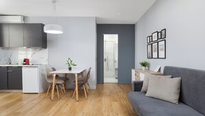 Eine moderne Küche mit integriertem Geschirrspüler, ein Essbereich mit Tisch und Stühlen, ein graues Sofa und ein Duschbereich.