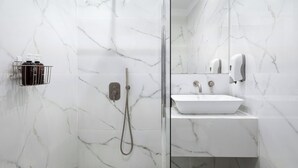 Ein modernes Badezimmer mit einer gläsernen Duschkabine, einem weißen Waschbecken und Marmorwänden.