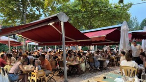 An outdoor dining area with tables and chairs, covered by red canopies, surrounded by trees. - House le Rouret (Grospierres)