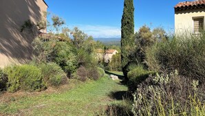 A hillside view with a tall cypress tree, a building with a tiled roof, and a clear blue sky. - House le Rouret (Grospierres)
