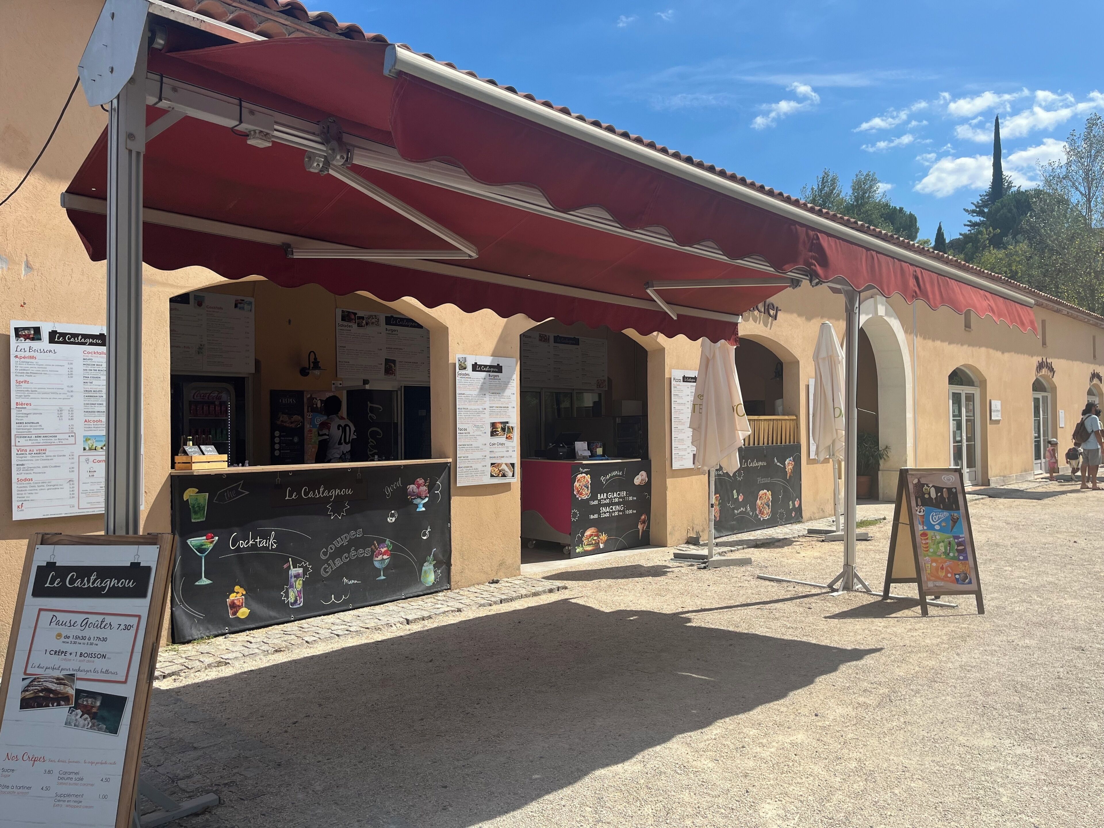 Un restaurante con terraza, carteles de menú y un toldo rojo.