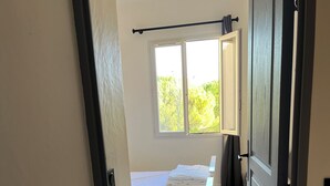 A narrow hallway leading to a room with two beds, a window with a view of greenery, and a door with a handle. - House le Rouret (Grospierres)