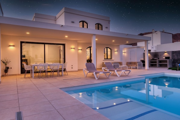 Ein modernes Haus mit Pool, Sitzgelegenheiten im Freien und einer überdachten Terrasse.