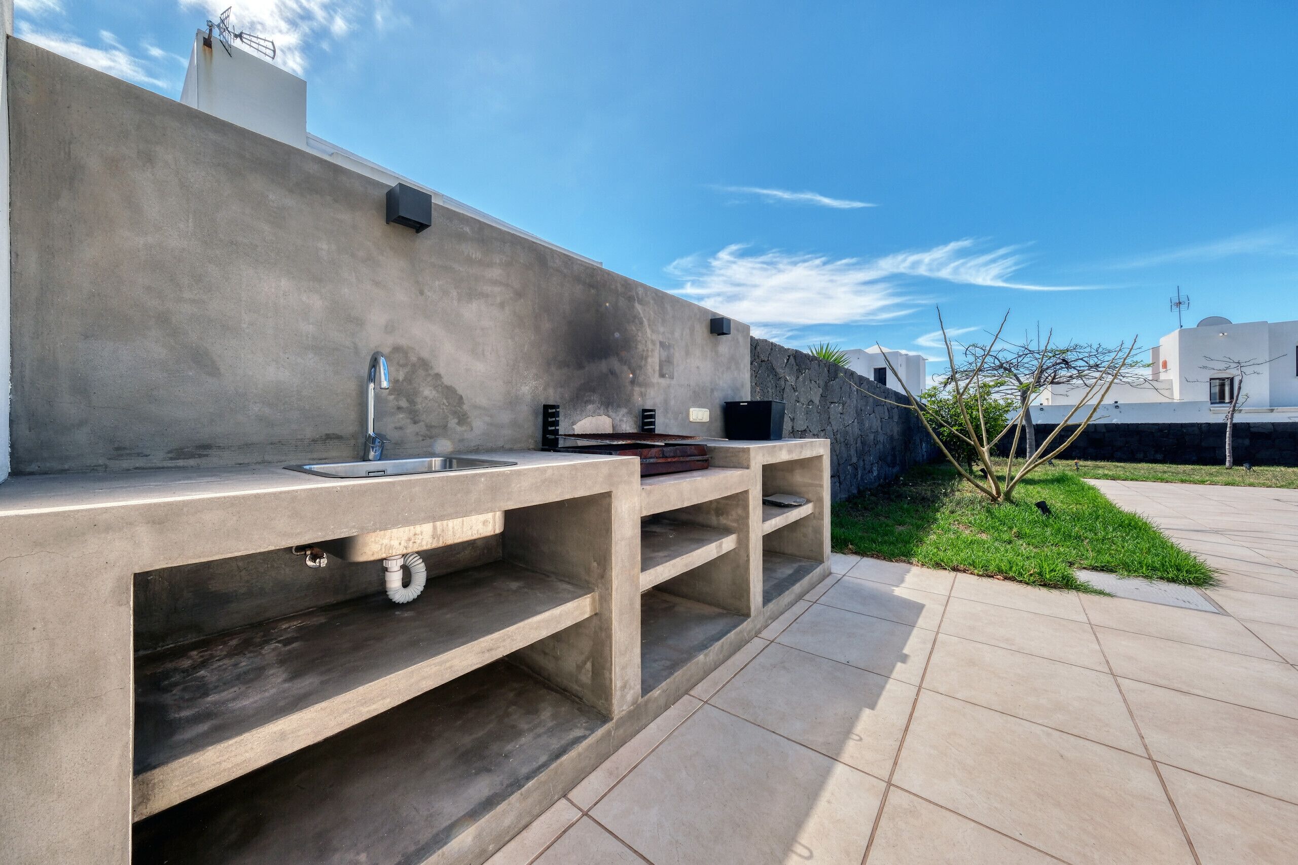 A concrete outdoor kitchen with a sink, a built-in stove, and a small shelf.
