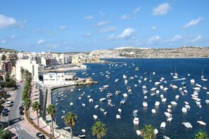 Un paysage urbain côtier avec un port de plaisance rempli de bateaux, une route bordée de voitures et des bâtiments le long du front de mer.