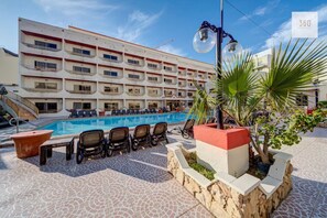 Un hôtel doté d’une piscine, de chaises longues et d’un palmier.