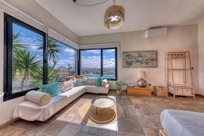 A modern living room with a large window, a sofa, a round coffee table, and a small wooden ladder. - Villa El Erizo • Pool • LVH (Nazaret)