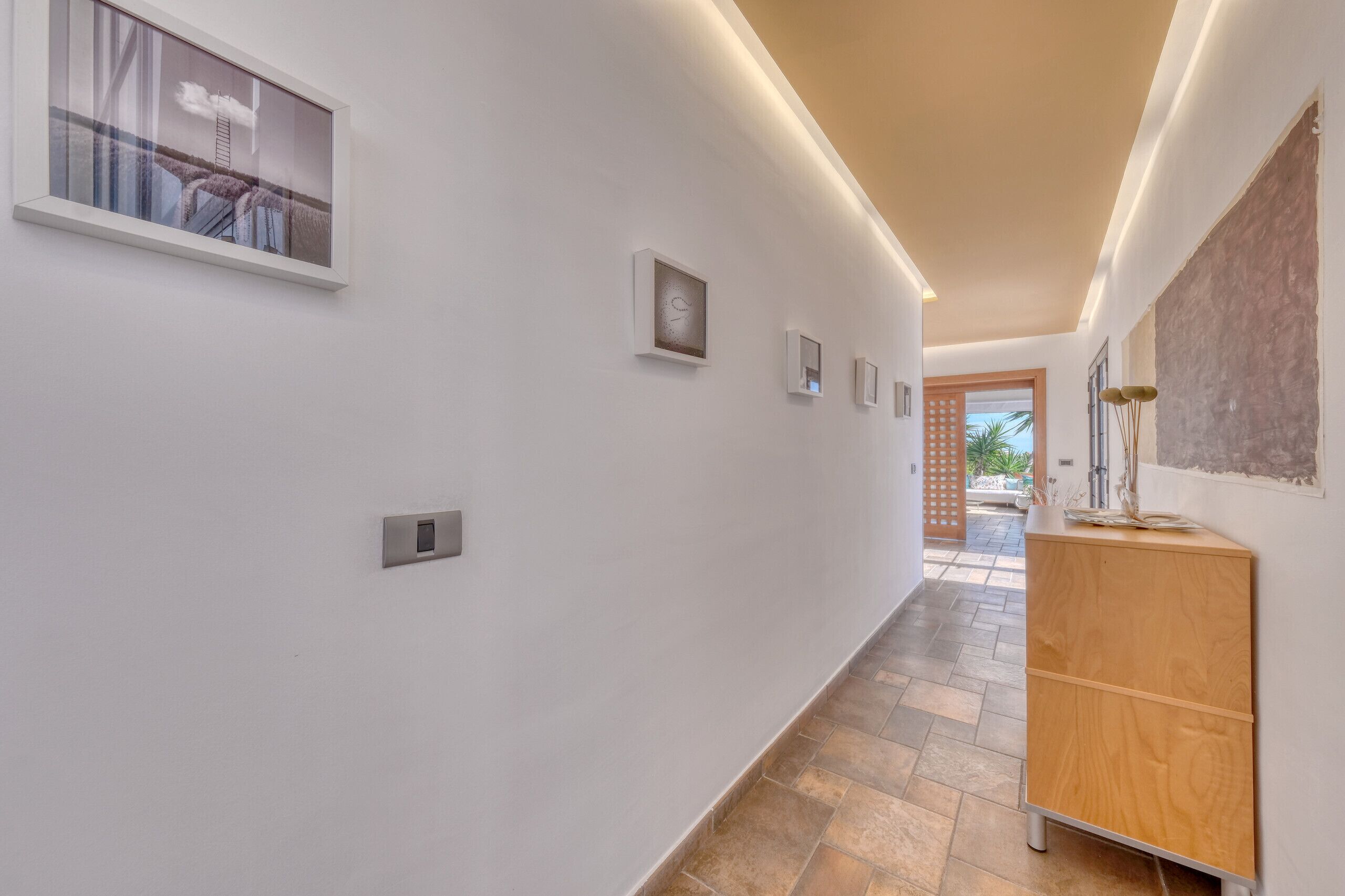 A hallway with a wooden cabinet, a window with a view, and a door leading to an outdoor area.