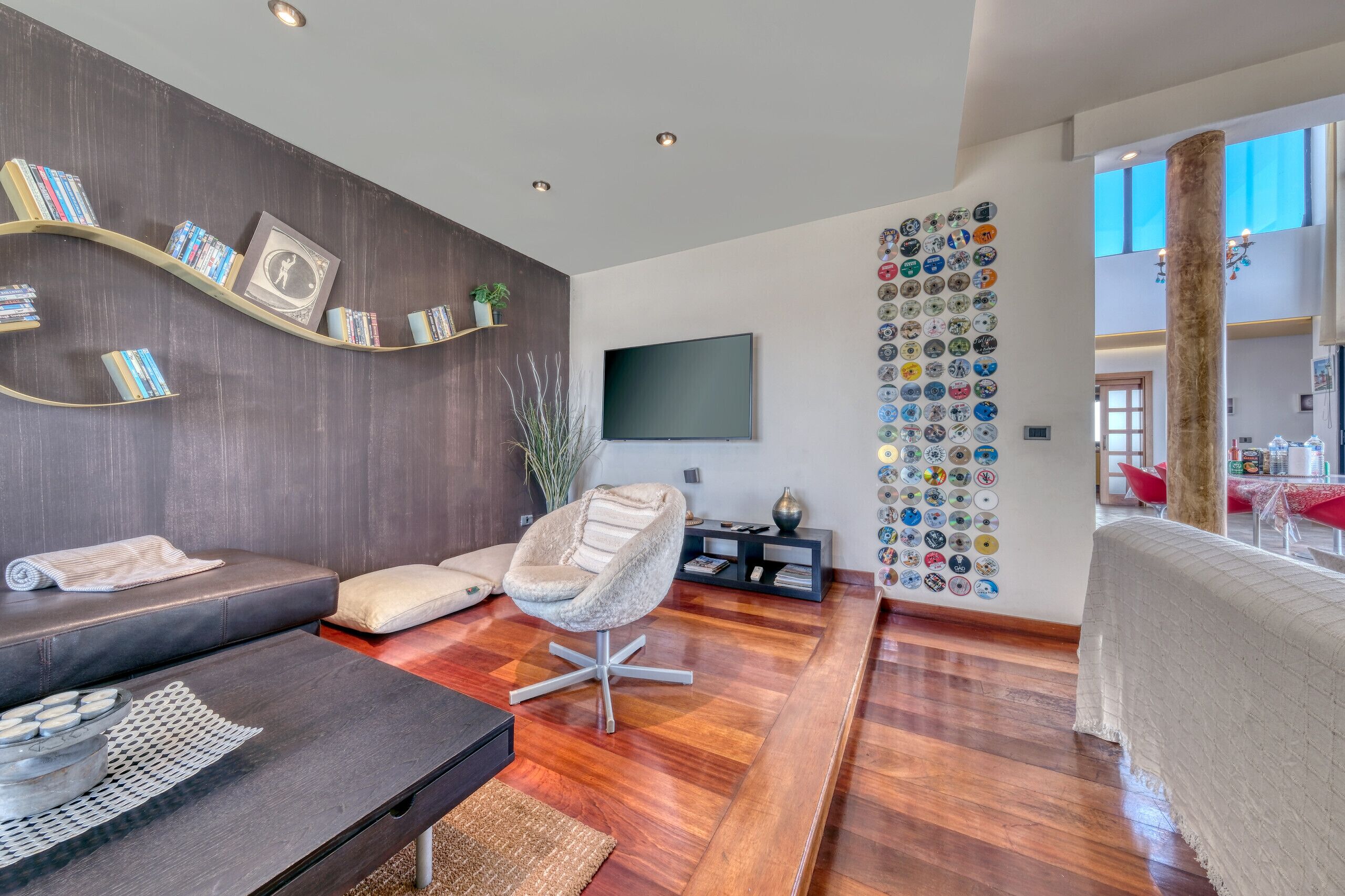 Een moderne woonkamer met een bank, een fauteuil, een flatscreen televisie, een wand met decoratieve borden en een houten vloer.