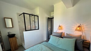 Ein Schlafzimmer mit Bett, Nachttischlampen, einem Fenster, einem Spiegel und einem Badezimmer mit Dusche.