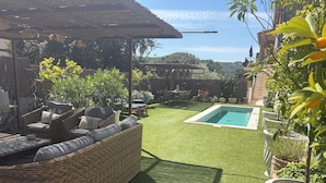 Ein Garten mit künstlichem Rasen, einem Pool, Korbmöbeln und Blumentöpfen.