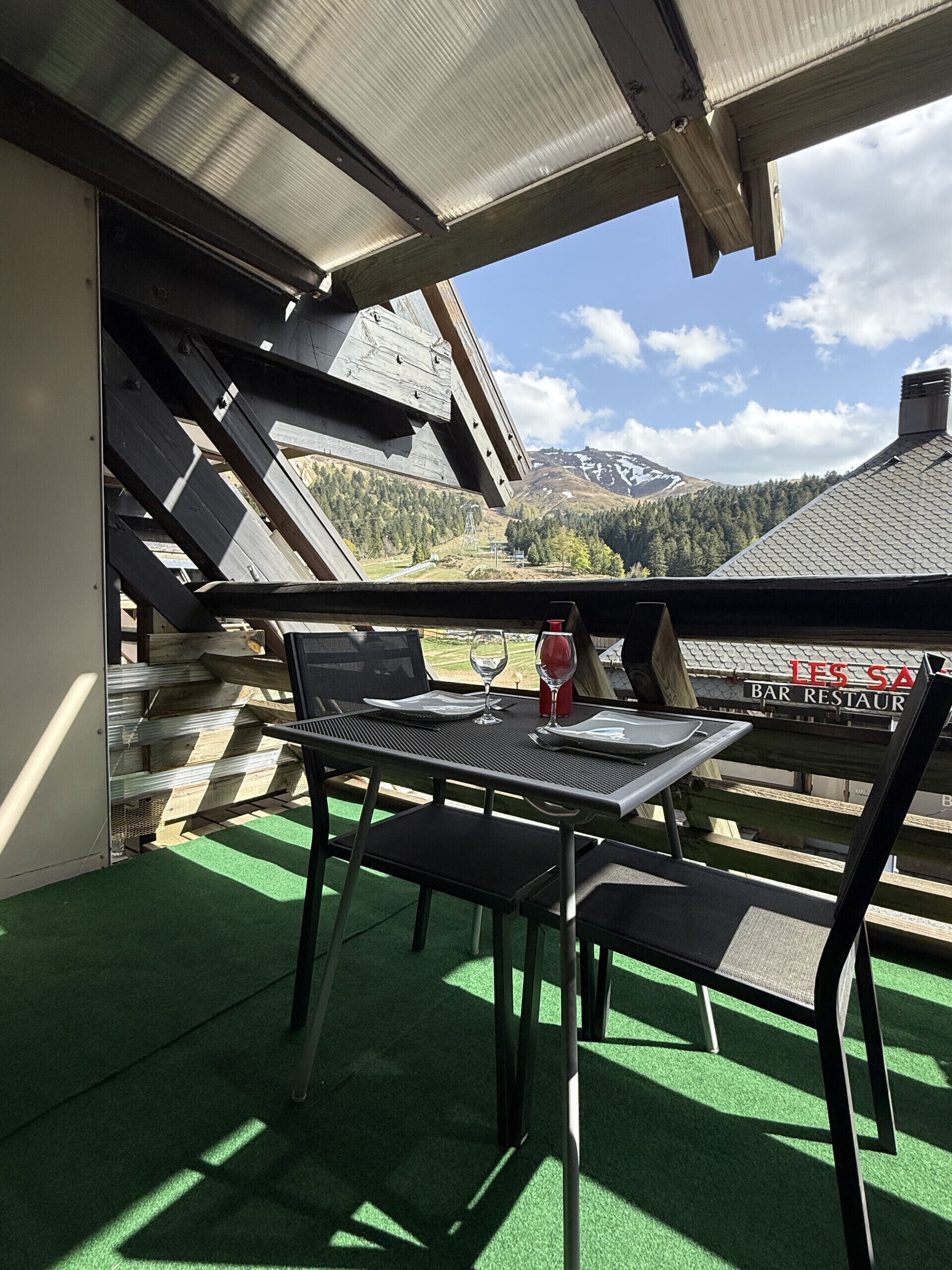En balkon med et bord, stole, en flaske og et glas vin.