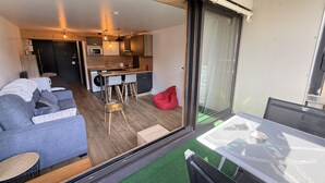 Een modern interieur met een bank, een glazen tafel, een rode loungestoel en een keukenruimte zichtbaar door een schuifdeur.