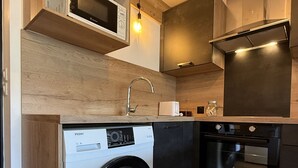 Een praktische keuken met een wasmachine, oven, magnetron en houten kastjes.