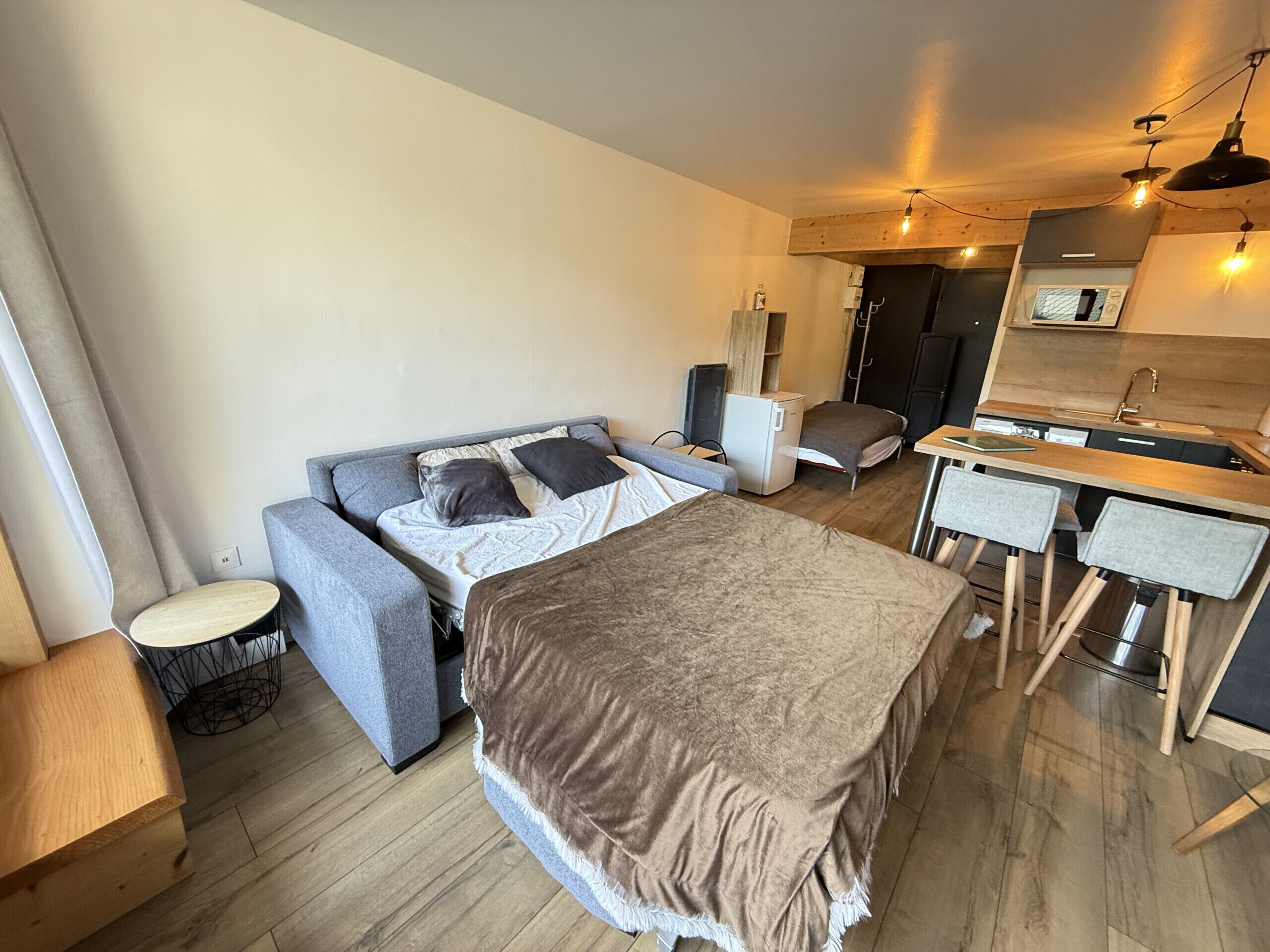 Une chambre d’hôtel compacte comprenant un lit, un canapé, un bureau, une chaise, une petite table et un coin cuisine.
