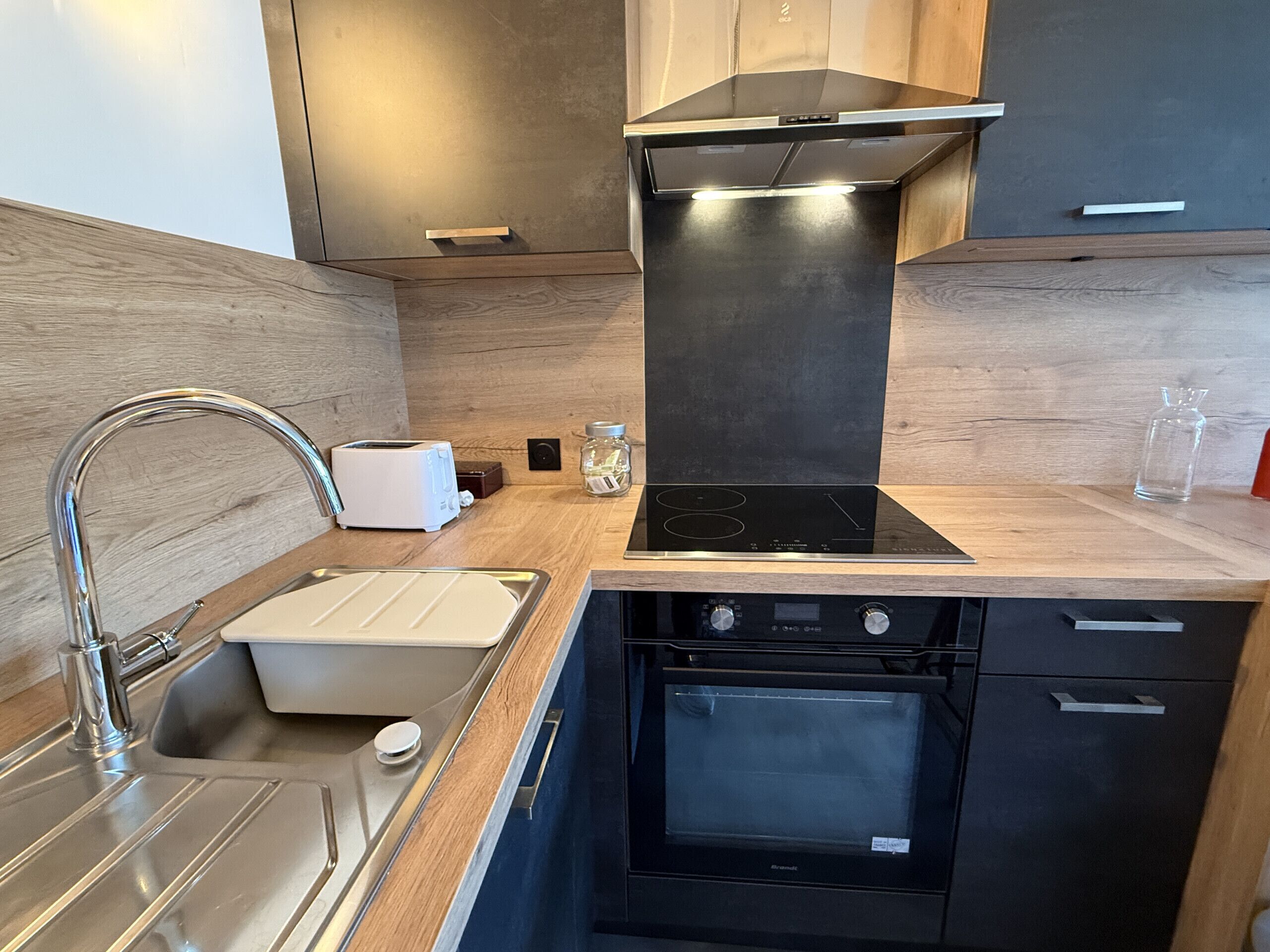 A modern kitchen with a stainless steel sink, a toaster, an oven, and a black range hood.