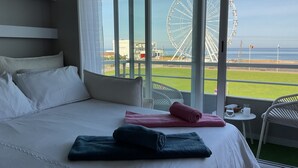 Ett hotellrum med en stor säng, utsikt över ett pariserhjul och en balkong med stolar.