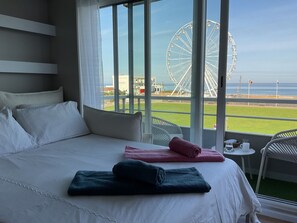 Ein Hotelzimmer mit einem großen Bett, Blick auf ein Riesenrad und einem Balkon mit Stühlen.