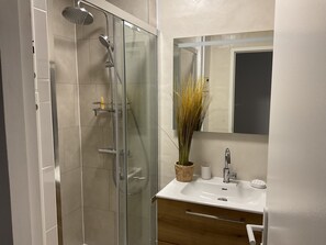 Uma casa de banho moderna com cabine de duche em vidro, uma sanita branca e um espelho em cima.