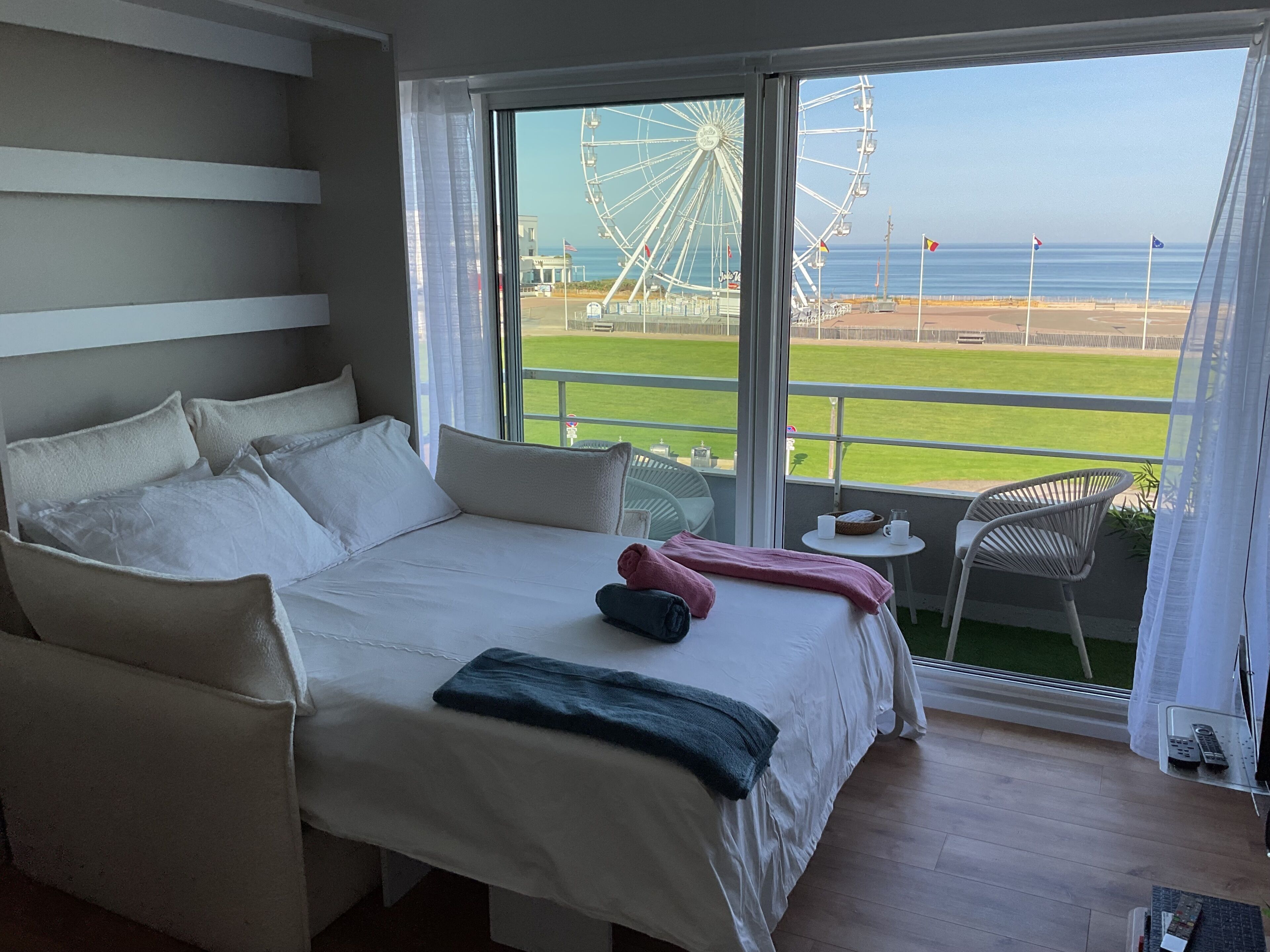 Une chambre avec un grand lit, une vue sur une grande roue et un balcon équipé d’une chaise et d’une table.