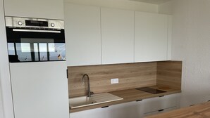 Ett modernt kök med vita skåp, en bänkskiva i trä, en inbyggd ugn och en blandare i rostfritt stål.