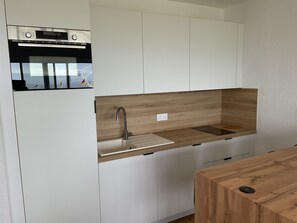 Eine moderne Küche mit weißen Schränken, einer Holz Arbeitsplatte, einem eingebauten Ofen und einem Edelstahl-Wasserhahn.