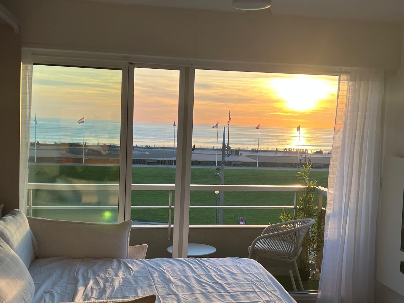 Een hotelkamer met een groot raam, met uitzicht op een sportveld en de zonsondergang.