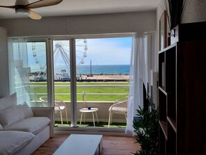 Ein Zimmer mit einer großen Schiebeglasdoor, die auf einen Balkon mit Blick auf das Meer und ein Riesenrad führt.