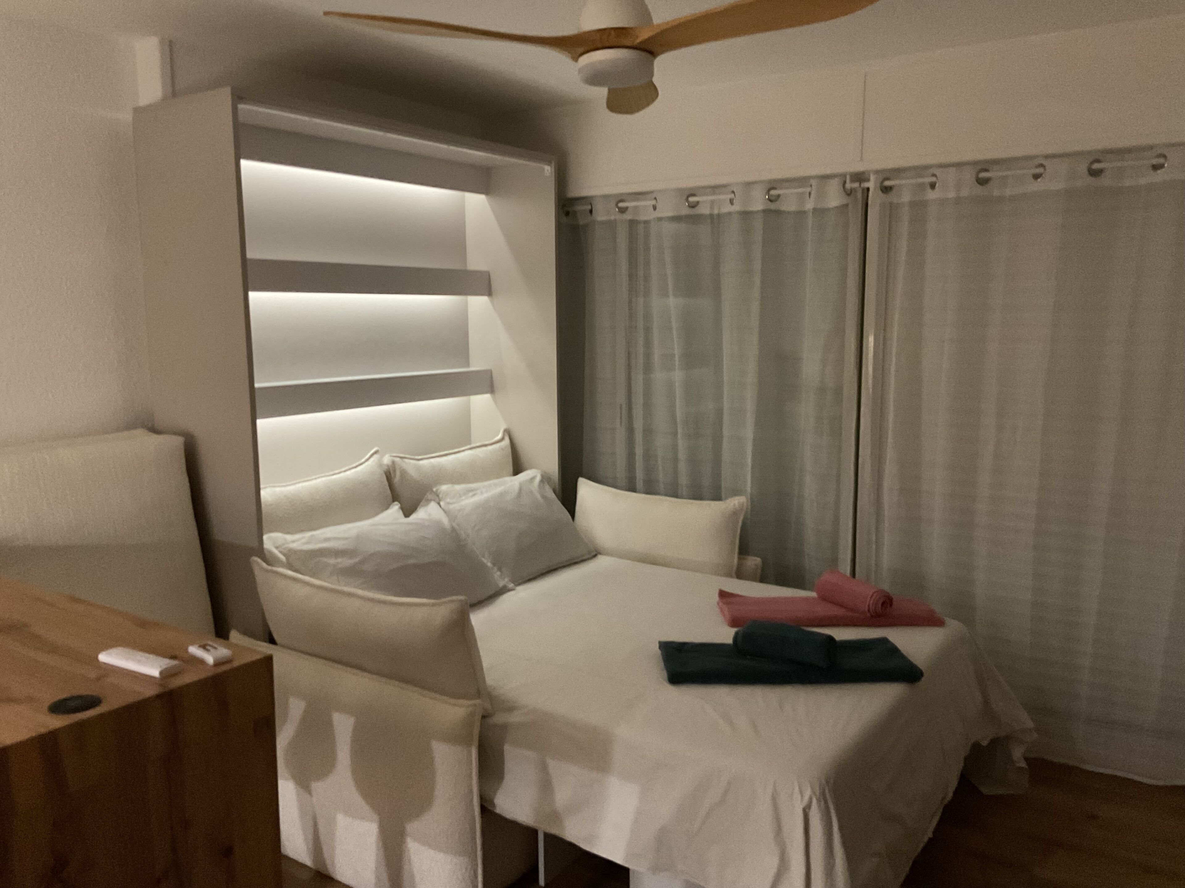 A modern bedroom with a bed, bedside tables, a ceiling fan, and a window with curtains.