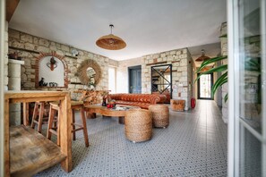 A spacious living area with a stone wall, a leather sofa, a wooden coffee table, and a patterned floor. - My Adress Alaçatı (Cesme)