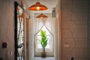 A hallway with a potted plant, a hanging light fixture, and a window with sheer curtains. - My Adress Alaçatı (Cesme)