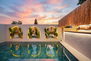 En swimmingpool med tre upplysta valv, ett halmtak och en bar.