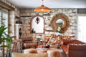 A rustic interior with stone walls, a wooden bench, a leather sofa, a hanging light fixture, and a mirror. - My Adress Alaçatı (Cesme)