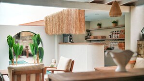 A dining area with a wooden table and chairs, a hanging light fixture, and a kitchen area with shelves and plants. - My Adress Alaçatı (Cesme)