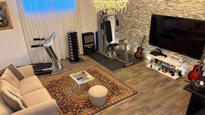 Ein Wohnzimmer mit einer Couch, einem Fernseher, einer Trainingsstation und einer Gitarre.