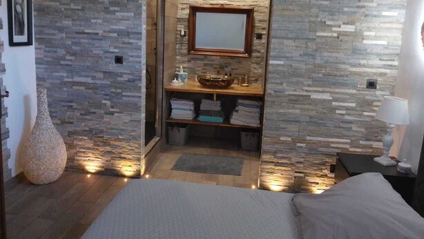 Ein Schlafzimmer mit Steinsturz, einem Holzwaschtisch, einem Spiegel und einem Bett.
