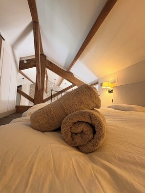 A bedroom with a sloped ceiling, wooden beams, a bed with white linens, and a wall-mounted lamp. - Charming apartment-comfort and elegance-St Rémy De Provence-5 mn from town center (Saint-Rémy-de-Provence)